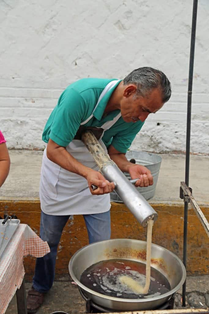 Gentleman pushing churro dough into a oil bath 