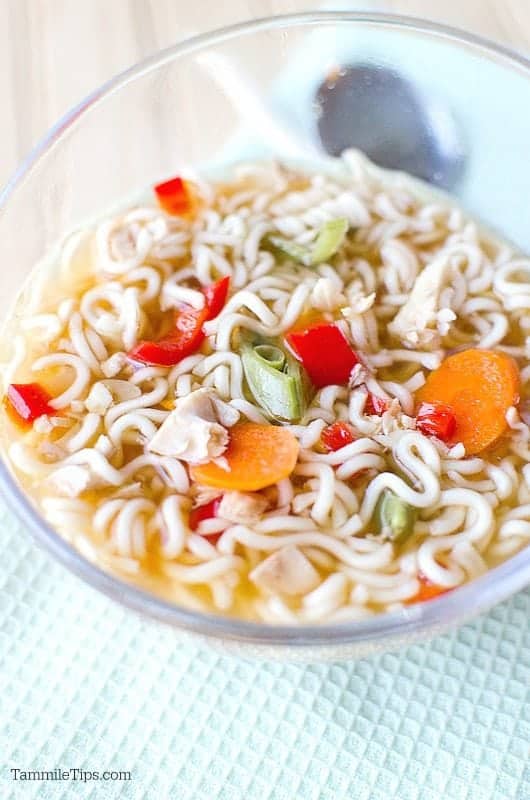 Chicken ramen soup in a glass bowl next to a spoon on a cloth napkin