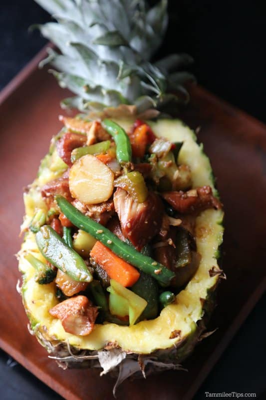 a pineapple filled with teriyaki chicken and vegetables on a wooden plate