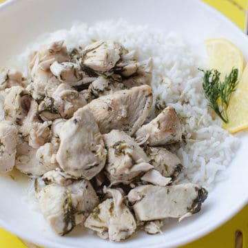 lemon dill chicken next to white rice and a lemon slice on a white plate