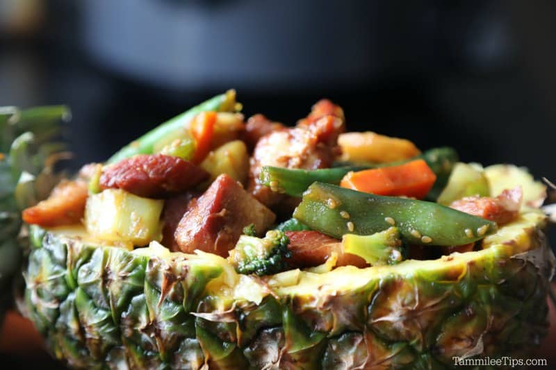 a pineapple filled with teriyaki chicken and vegetables on a wooden plate