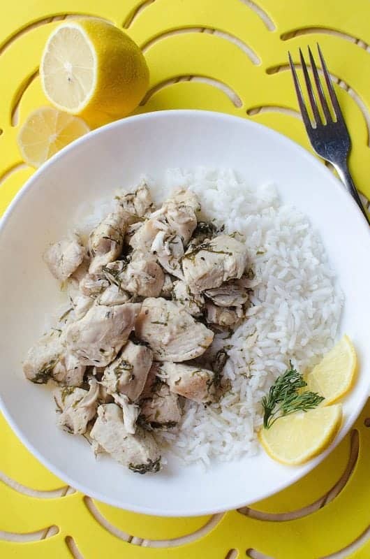  a white plate with chicken, rice, and lemon slices next to a fork and lemon pieces