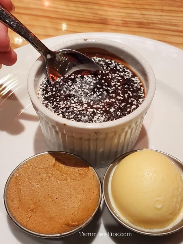 Spoon going into chocolate cake in a white ramekin next to small containers of peanut butter and ice cream