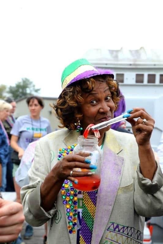 Women dressed in mardi gras colors holding a gummy worm out of a mason jar