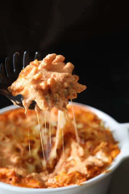 Dark pasta server scooping ziti and cheese out of white baking dish