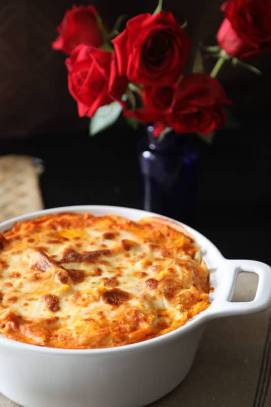 baked cheese dish next to a vase of roses