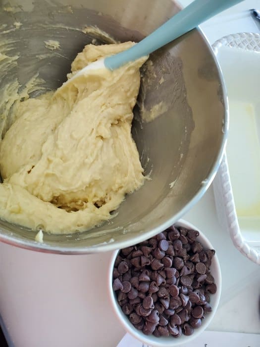 Banana bread batter in a metal bowl with a spatula next to a bowl of chocolate chips 