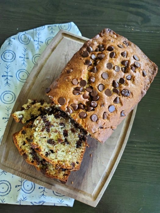 Chocolate chip banana bread sliced on a wooden cutting board next to a cloth napkin 