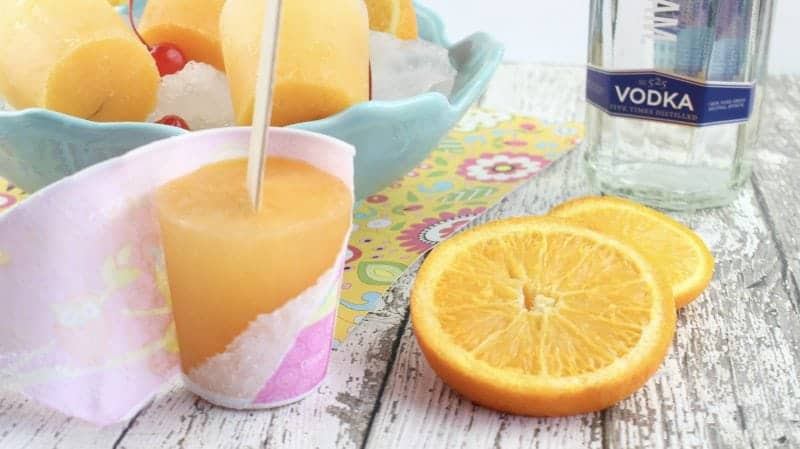 Screwdriver Popsicles next to oranges and a bottle of vodka