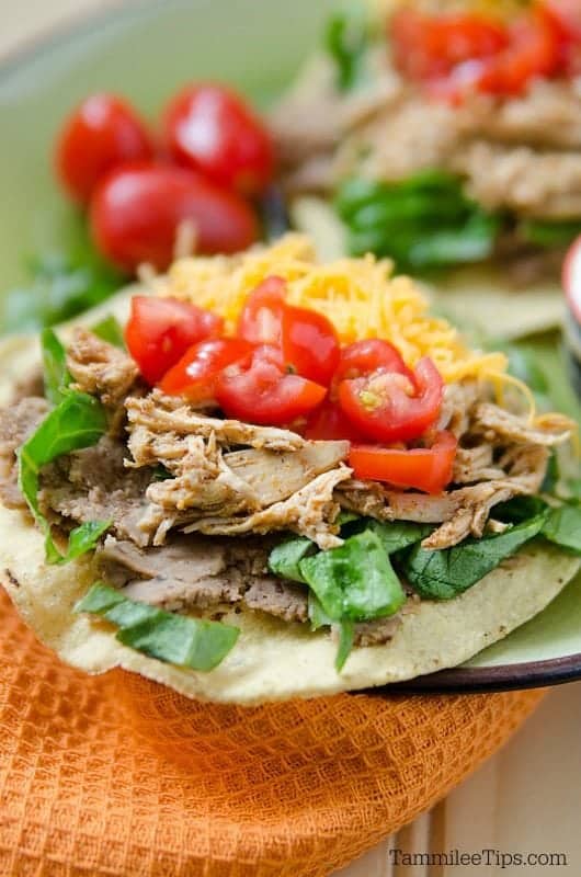 a plate with tostadas piled with chicken, tomatoes and cheese. 