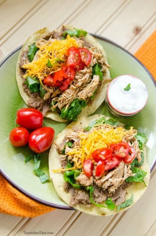 Crockpot chicken Tostada over a plate with tostadas piled with chicken, tomatoes and cheese. 