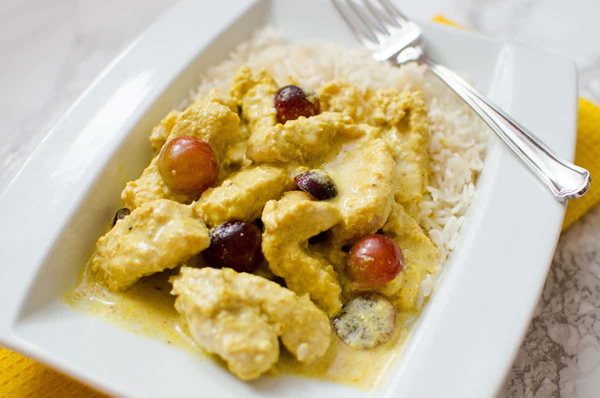 turkey curry with grapes on a white plate with a fork