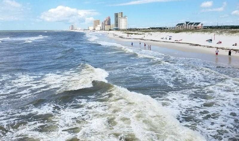 View of the water with people walking the beach and large buildings in the background