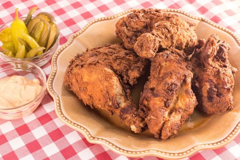 Nashville Hot Chicken on a yellow plate next to peppers and pickles