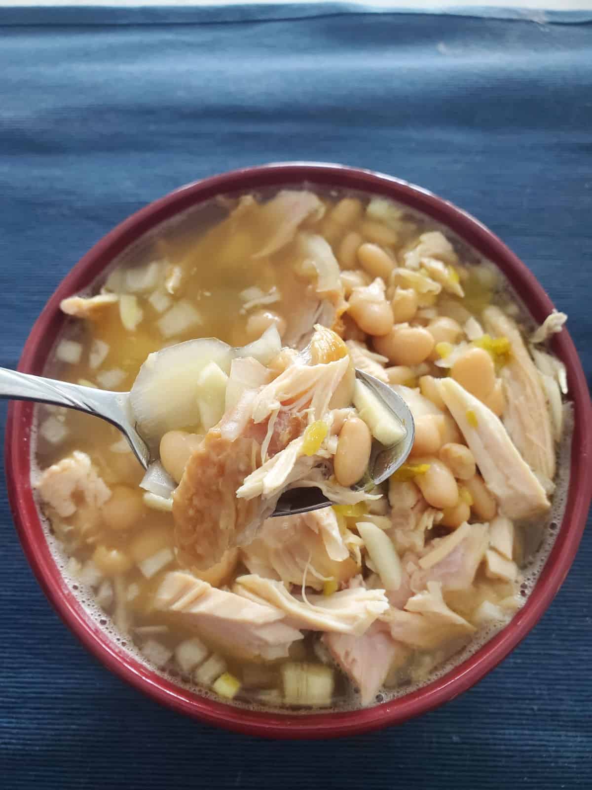 Spoon holding chicken and beans above a bowl of chili