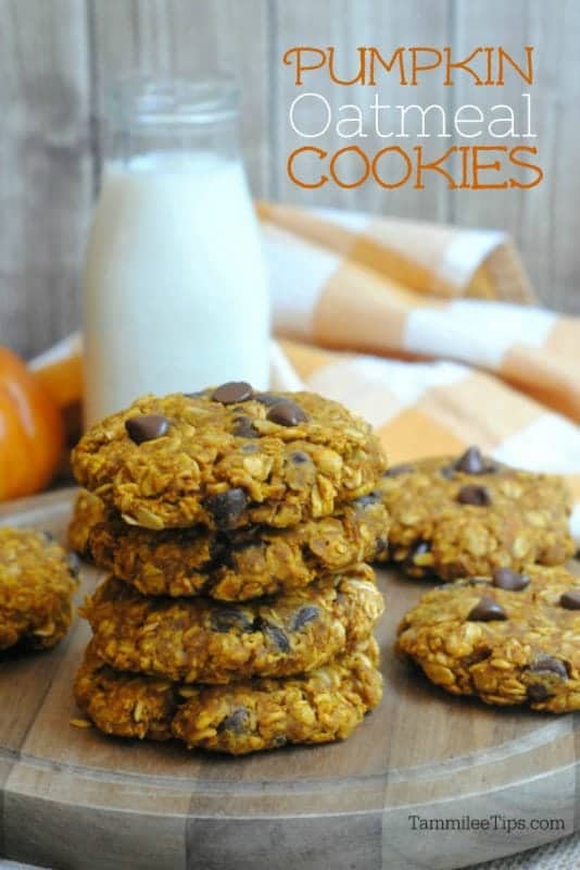 Pumpkin oatmeal cookies over a stack of cookies on a wooden board next to a pumpkin and glass of milk 