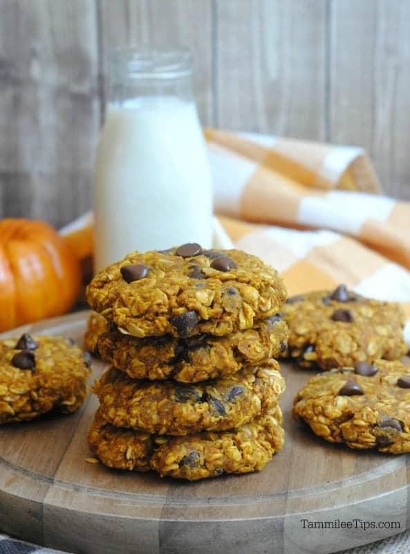 Stack of oatmeal cookies on a wooden board with a pumpkin and glass of milk in the background