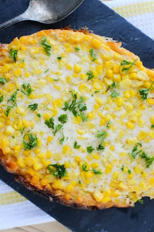 Crockpot Corn Pudding with a green garnish on a dark background with a silver spoon. 