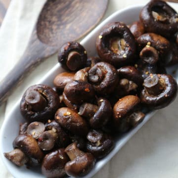 crockpot mushrooms on a white serving dish with a wooden spoon