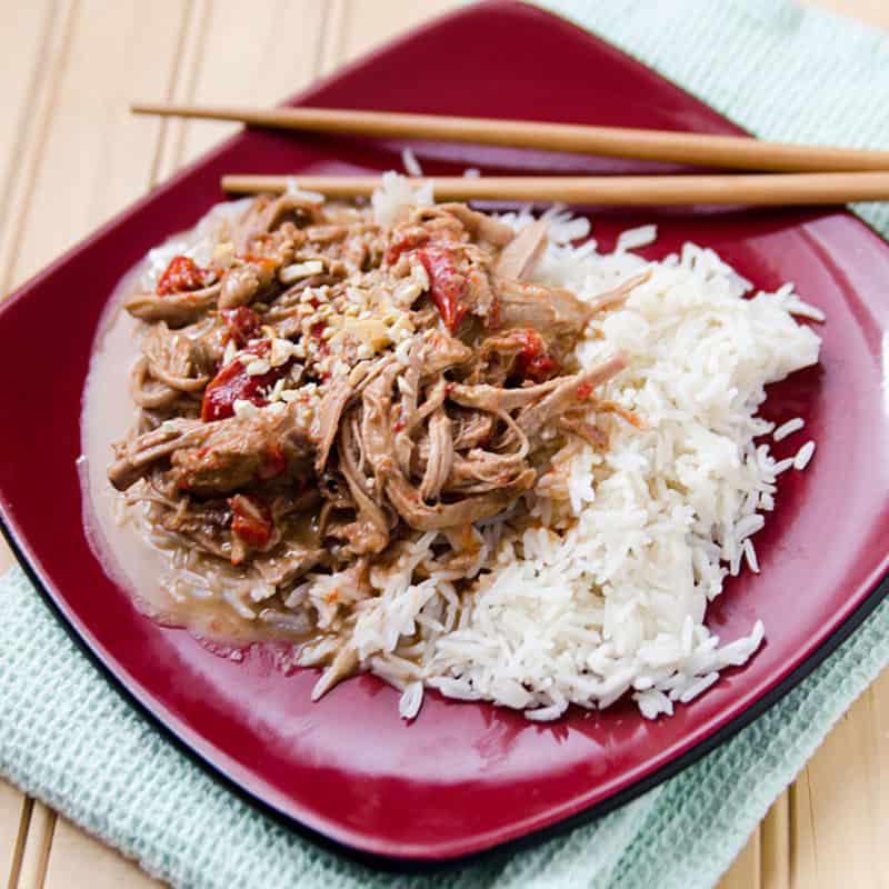 red plate with Thai pork and rice next to chopsticks