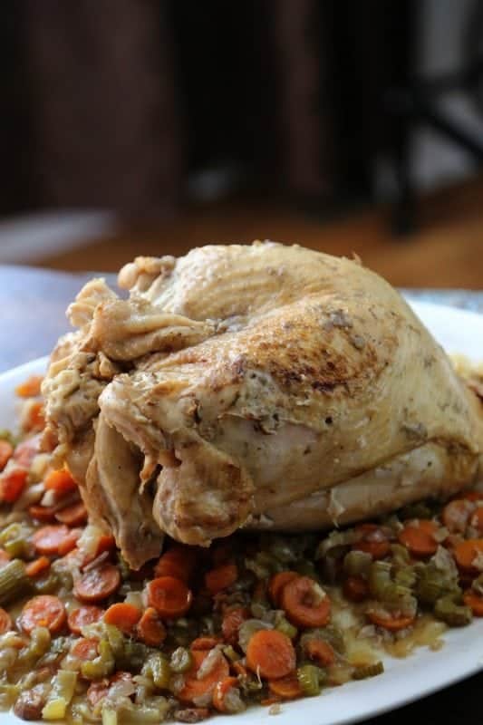crockpot turkey recipe on a white platter with carrots, celery, and onions under it