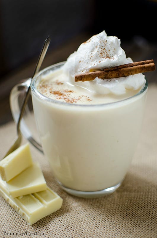 white hot chocolate garnished with whipped cream and a cinnamon stick in a glass coffee mug