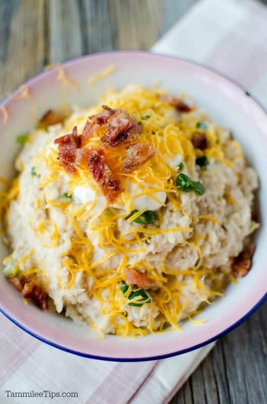 Close up of slow cooker cauliflower mashed and topped with bacon pieces, shredded cheddar cheese, green onions and sour cream. 