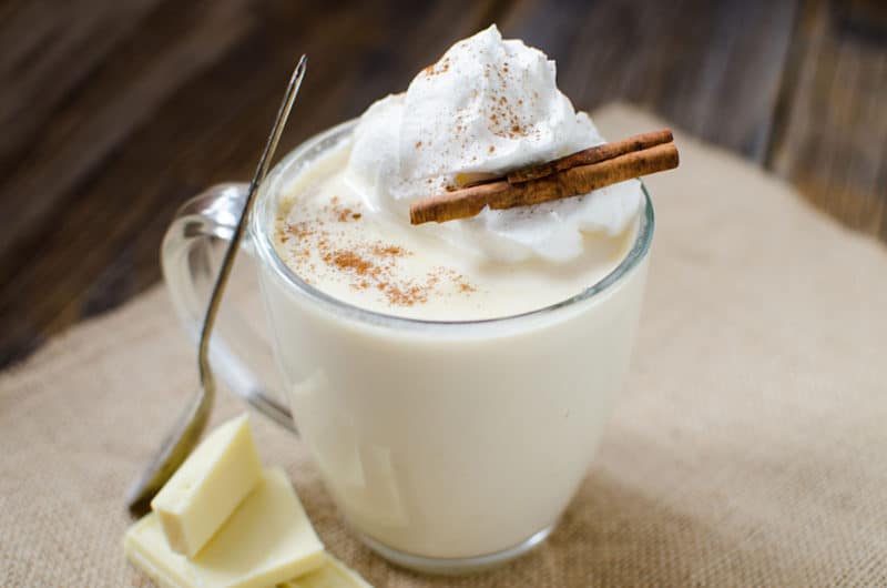 white hot chocolate in a glass mug garnished with whipped cream and a cinnamon stick