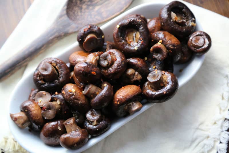 mushrooms in crock pot spread in a white bowl with a wooden spoon. 