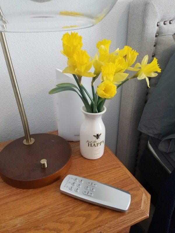 LulaaBed remote next to a vase of daffodils and a lamp on a nighstand