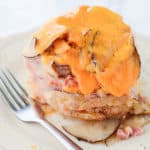 cheese melting over scalloped potatoes and ham on a white plate with a silver fork.