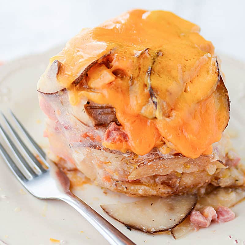 cheese melting over scalloped potatoes and ham on a white plate with a silver fork.