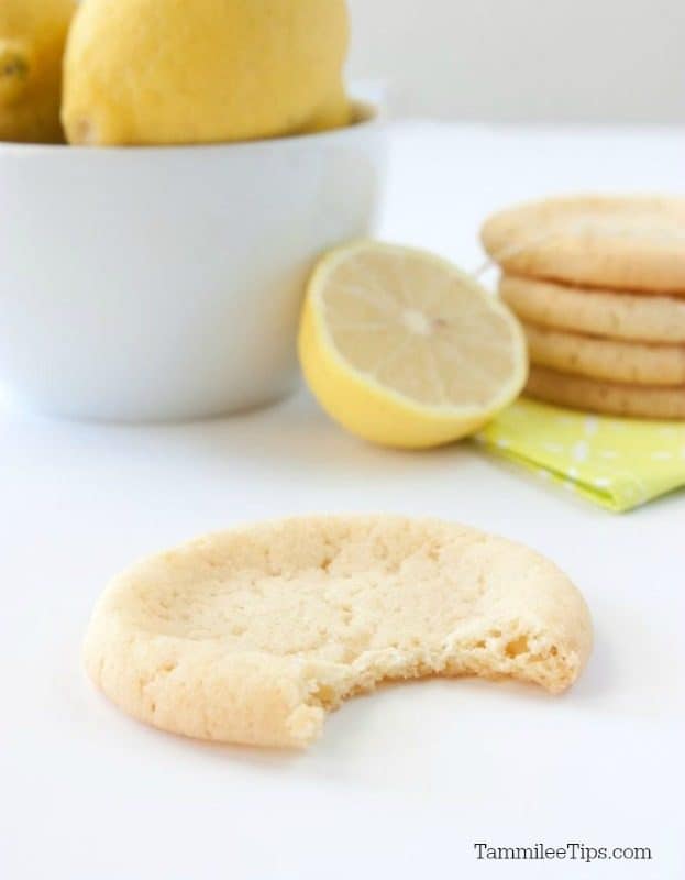 Cookie with a bite out of it next to a bowl of lemons and stack of cookies