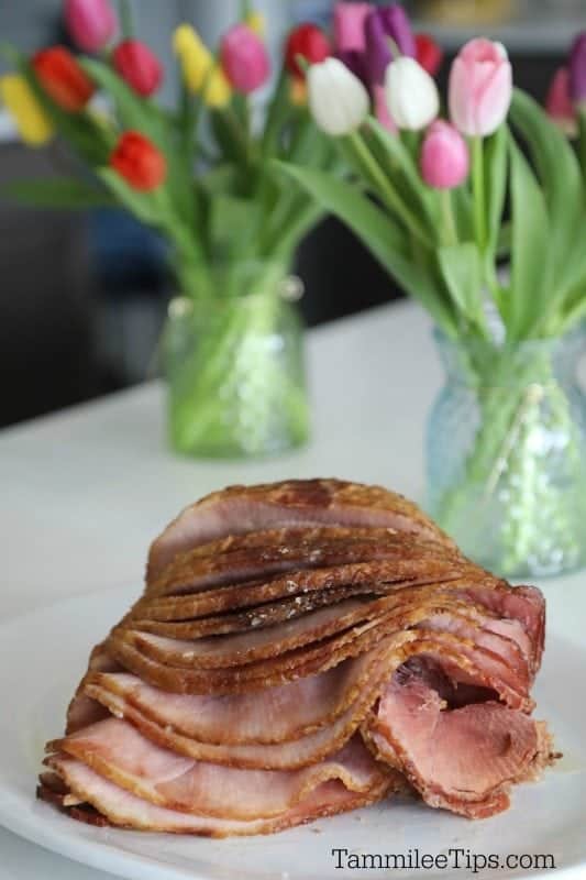 Spiral Ham on a white platter with vases of tulips in the background