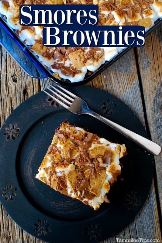 Smores brownie square on a blue plate with a fork next to it, top of the photo is the brownies in a baking pan on a wood background