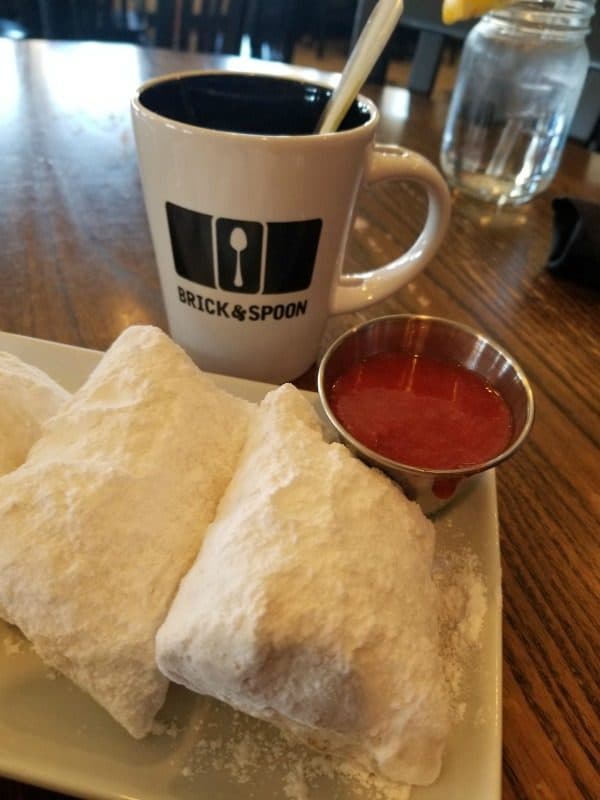 Beignets covered in powdered sugar next to a Brick and Spoon coffee cup