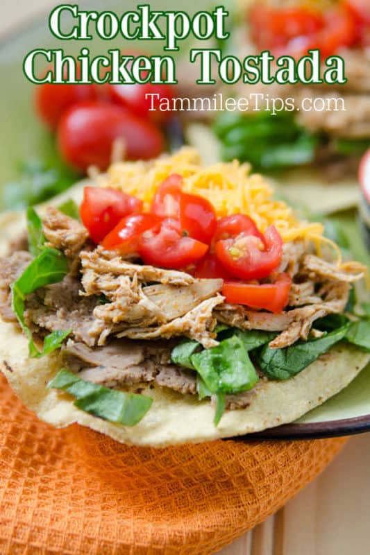 Crockpot chicken Tostada over a plate with tostadas piled with chicken, tomatoes and cheese. 