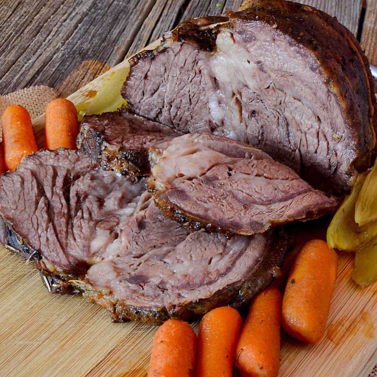 Crockpot roast sliced on a cutting board with carrots