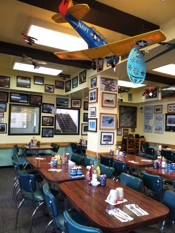 Airplane photos and model airplanes hanging from the ceiling over tables and chairs