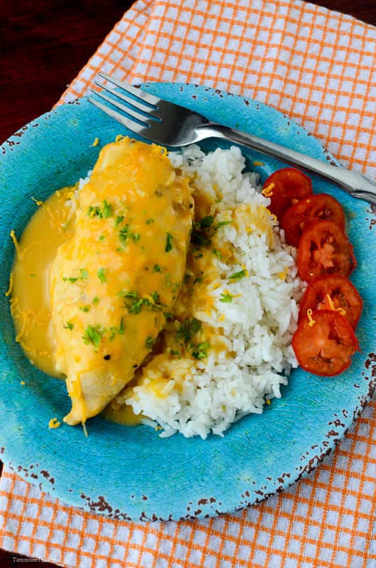 Cheesy Chicken and Rice on a blue plate with sliced tomatoes on top of an orange cloth napkin
