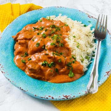 Chicken Tikka Masala next to white rice on a blue plate on a yellow cloth napkin