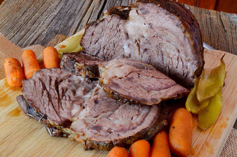 Sliced roast on a wooden cutting board with mini carrots