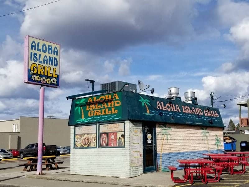 Aloha Island Grill sign next to a building with red picnic tables