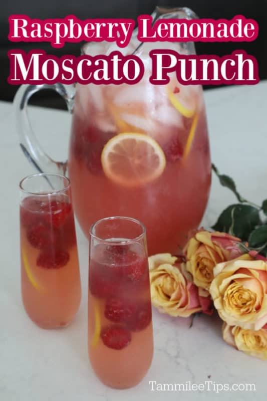 Raspberry Lemonade Moscato Punch over a glass pitcher and glasses with punch, raspberries and lemons next to roses