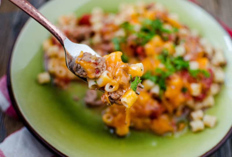 Fork holding cheeseburger pasta casserole over a green plate