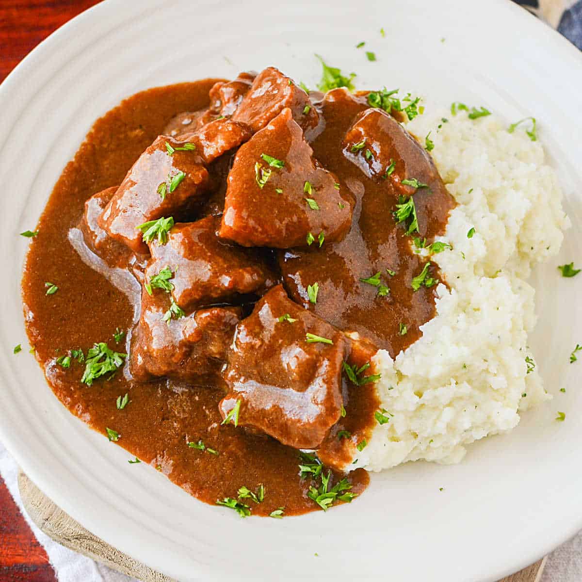 Crockpot Beef Tips and gravy next to potatoes on a white plate