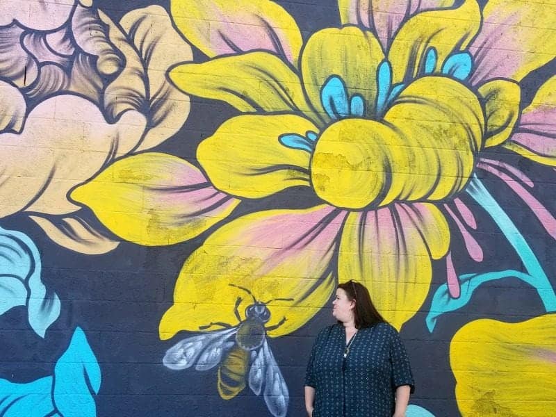 tammilee standing by a bee and flower mural