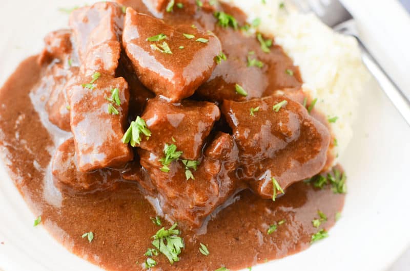 beef tips smothered in gravy next to mashed potatoes on a white plate