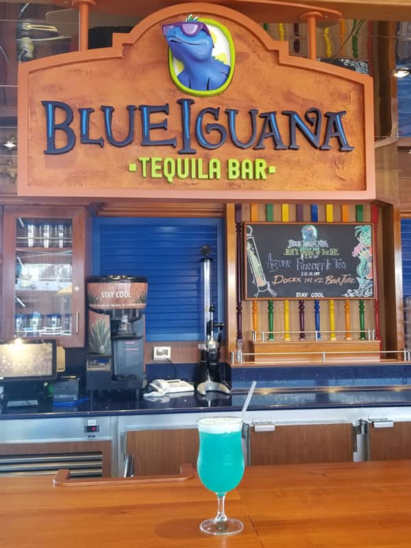 Blue margarita in a cocktail glass below a Blue Iguana Tequila Bar Sign 