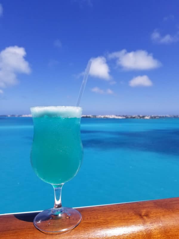 Blue margarita in a hurricane glass with the tropical ocean in the background